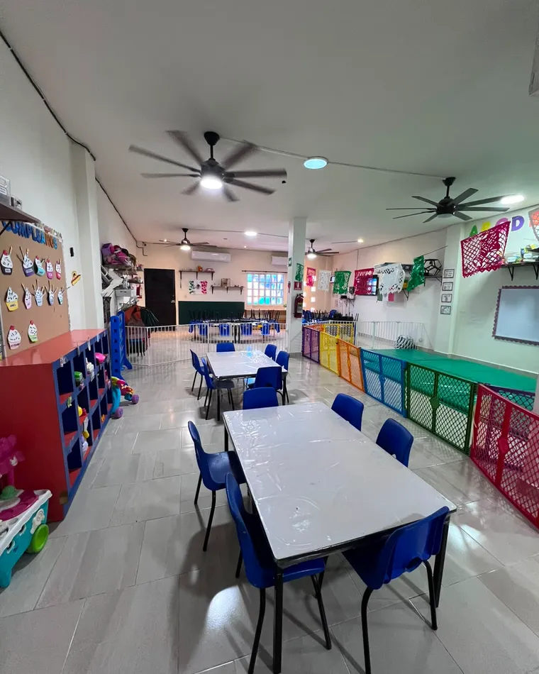 Salón de maternal con mesas pequeñas, sillas y materiales organizados.